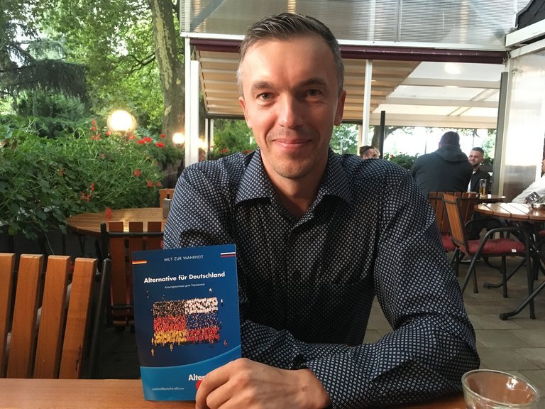 Eugen Schmidt von der AfD sitzt mit einer AfD-Broschüre an einem Restaurant-Tisch