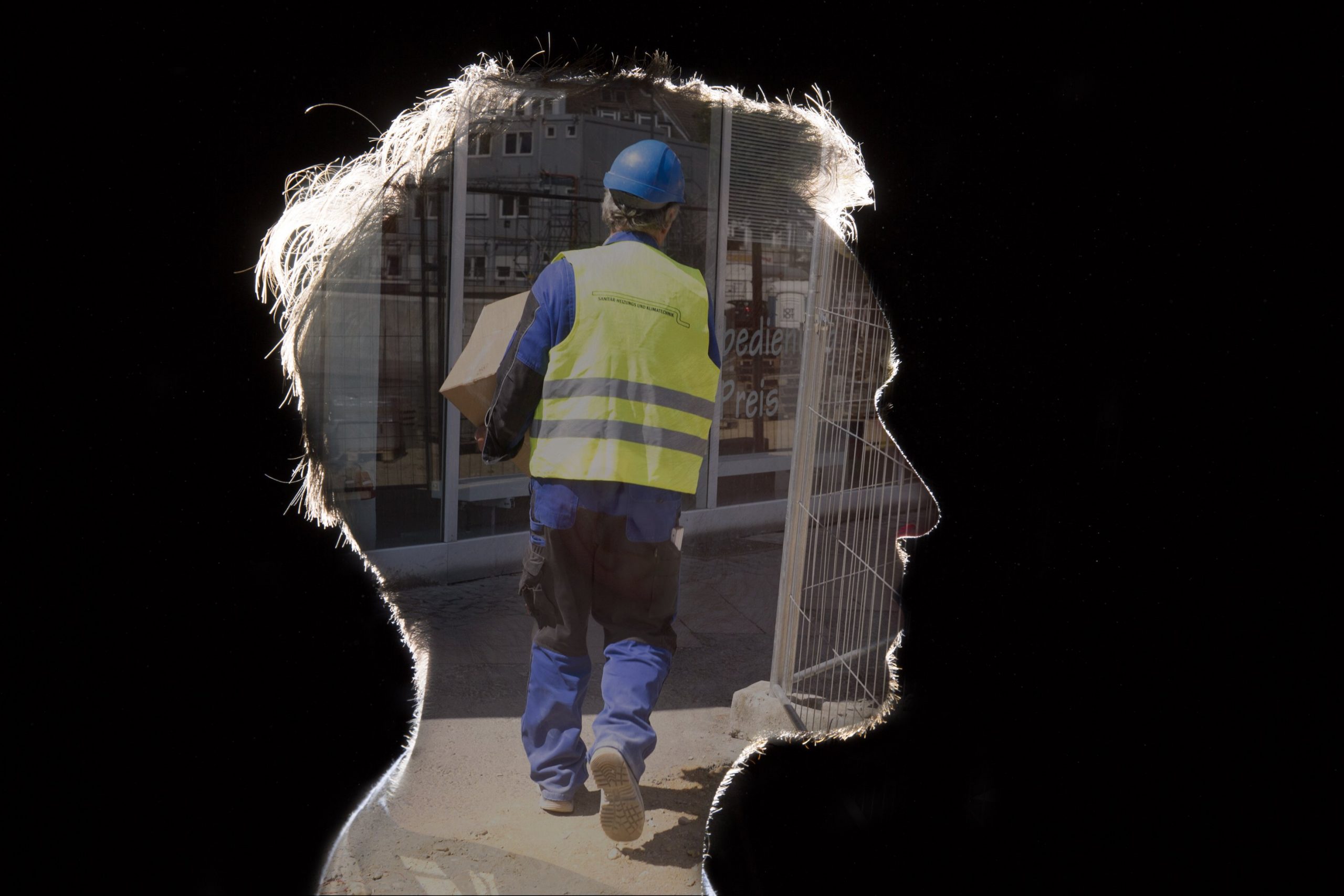 Ein Arbeiter, der eine Kiste trägt, umrahmt von der Silhouette eines männlichen Kopfs