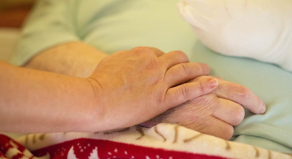 Eine Hand einer jüngeren Person liegt auf der Hand einer älteren Person