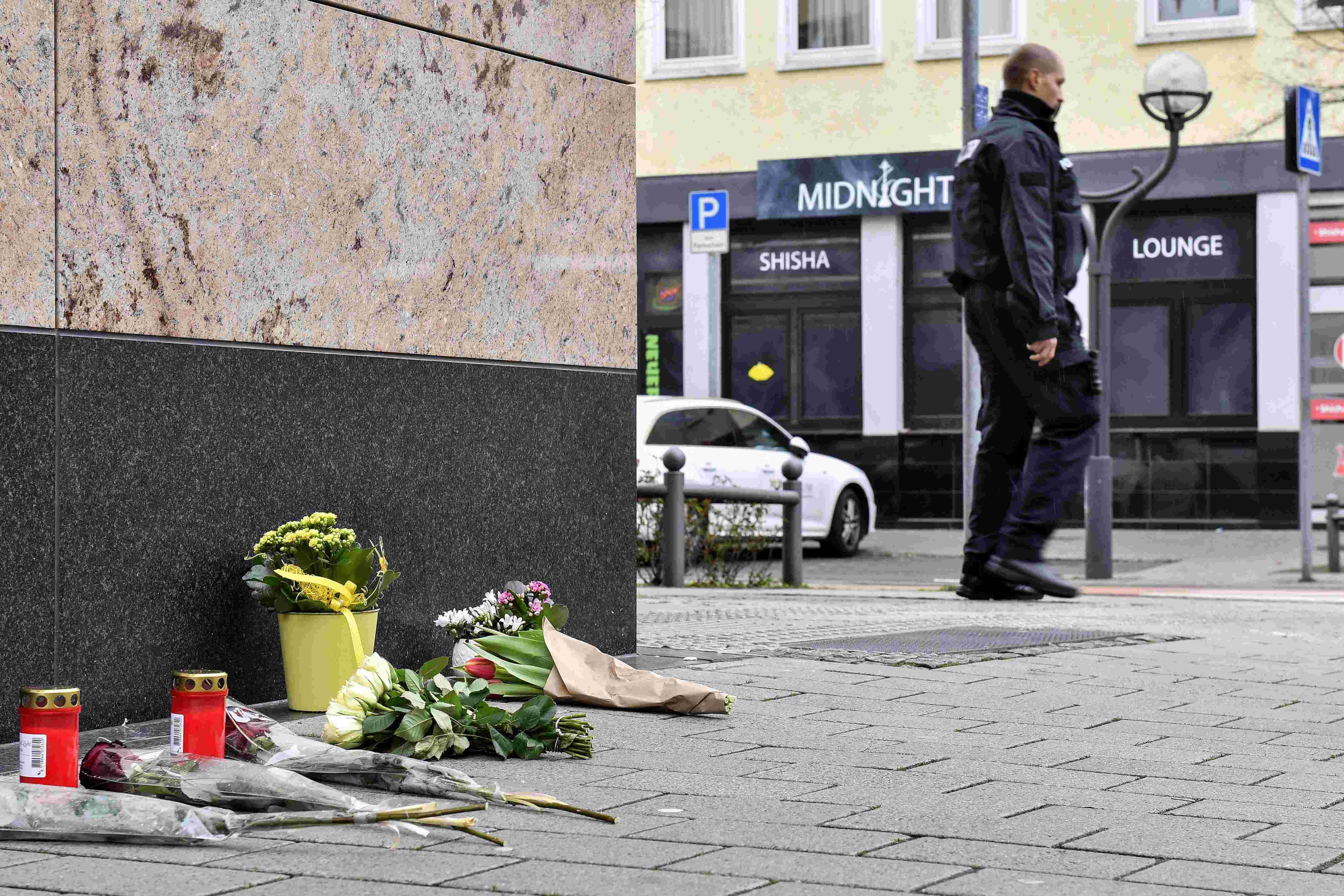 Auf dem Foto ist die Shisha-Bar "Midnight" in Hanau zu sehen, in der der 43-jährige Tobias R. seinen Anschlag startete. Im Vordergrund liegen Blumen auf dem Boden. Außerdem ist ein Polizist zu sehen, der gerade weggeht.