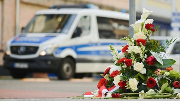 Anschlag in Hanau: Blumengesteck und im Hintergrund ein Polizeiwagen