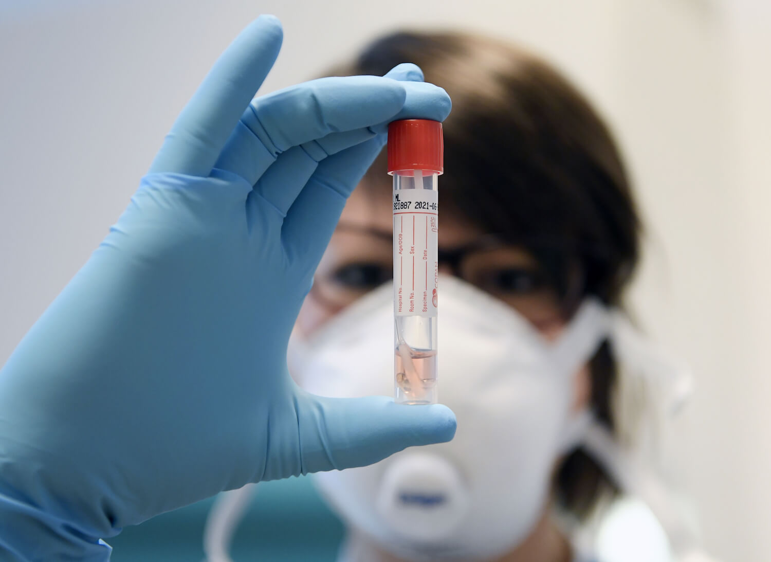 Eine Frau mit Mundschutz hält eine Proberöhrchen im Labor hoch