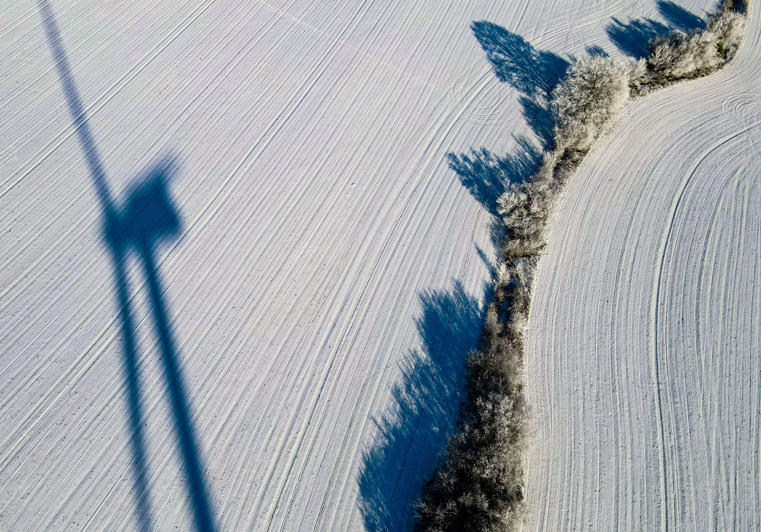 Foto, das den Schatten eines Windrades auf einem schneebedeckten Acker zeigt.