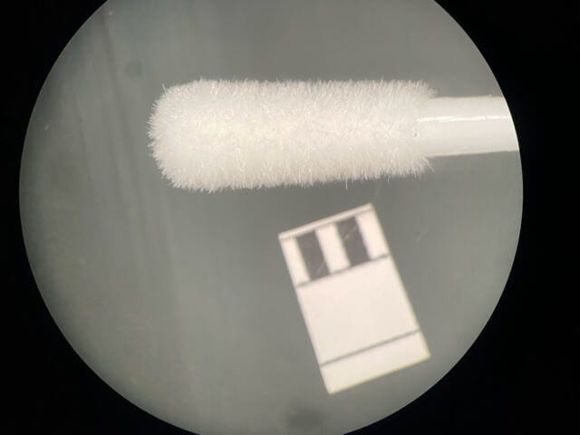 Das Teststäbchen des ersten von uns untersuchten Schnelltests unter dem Mikroskop. Einzelne Fasern lösen sich. (Foto-Credit: Mark Benecke/ virusonline.de)