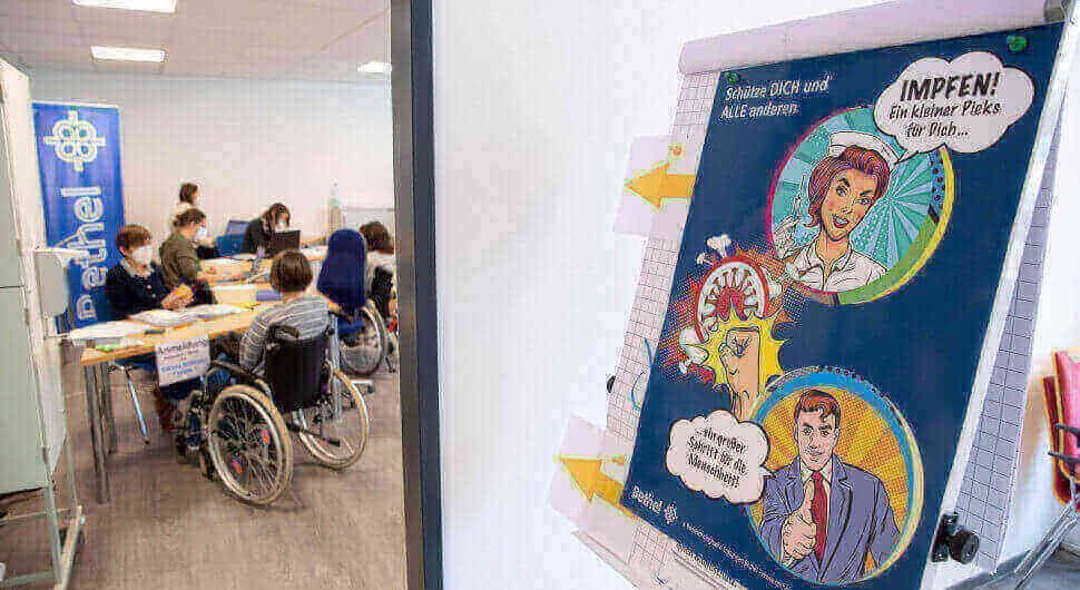 Menschen warten in einem impfzentrum auf eine Corona-Impfung, vor der Tür steht ein impffreundlicher Comic