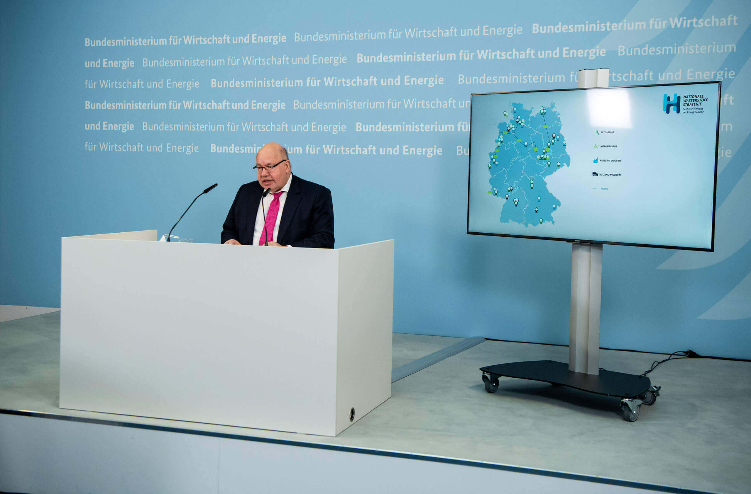 Bundeswirtschaftsminister Peter Altmaier sitzt vor einer Karte mit Standorten für ein EU-Wasserstoffprojekt: