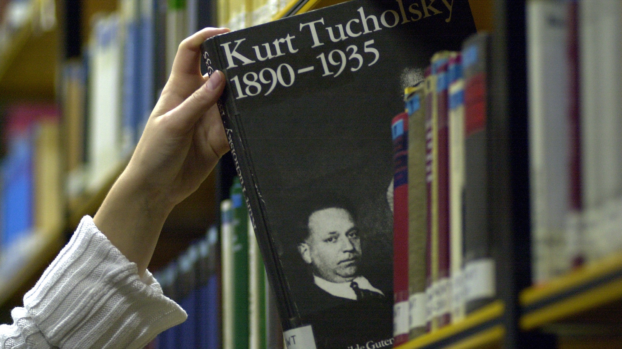 Jemand nimmt eine Biografie von Kurt Tucholsky aus einem Bücherregal.