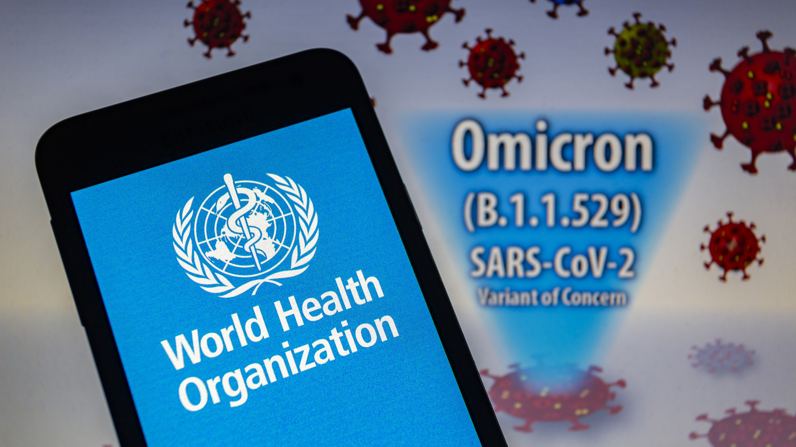 Smartphone mit WHO-Logo, Schriftzug Omikron-Variante und stilisierten Coronaviren.