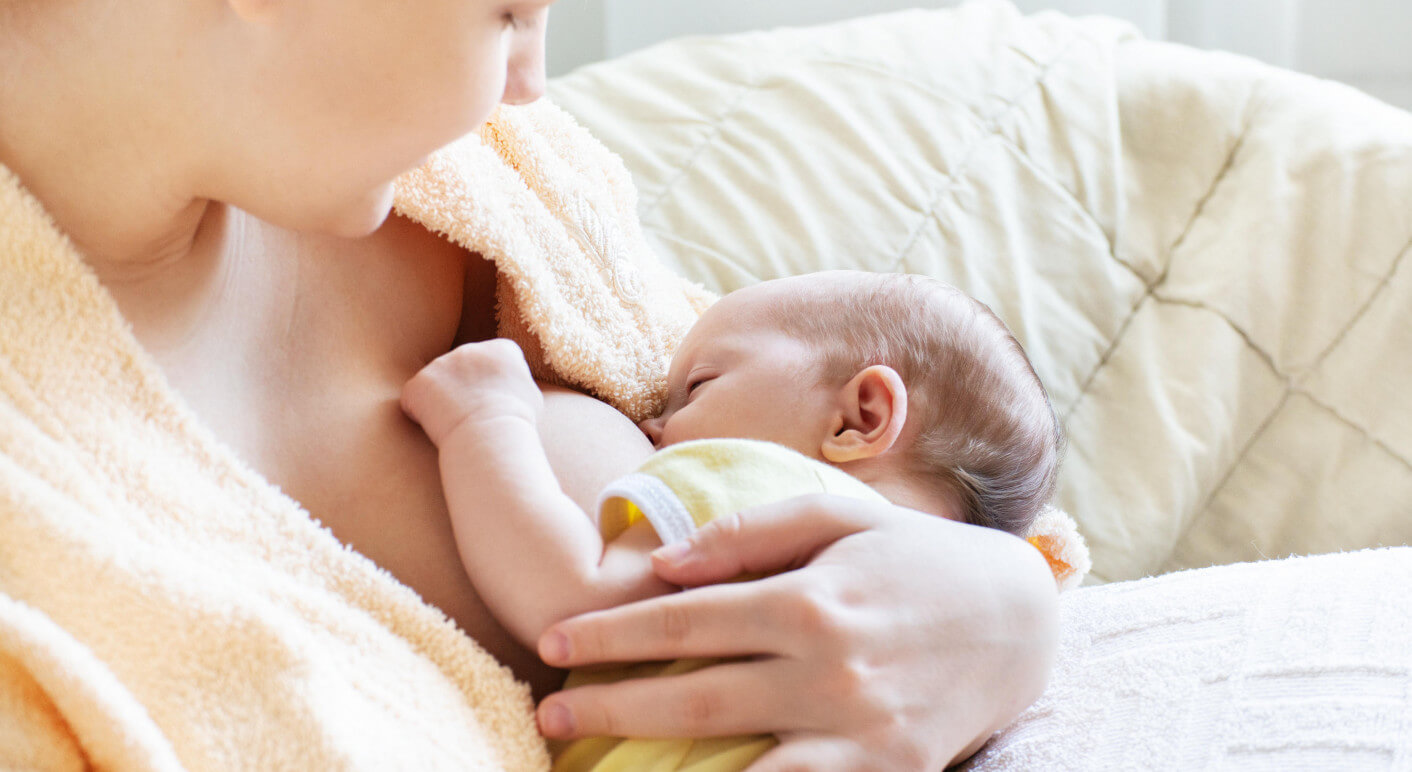 Baby eating breast milk. Caucasian blonde young mother breastfeeding her baby horizontal photo. Concept of lactation.