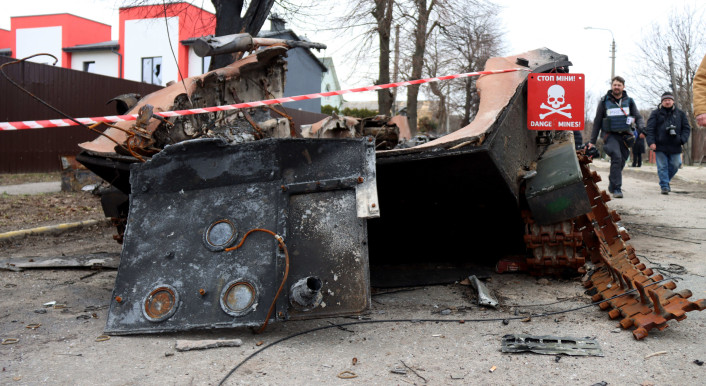 An einem zerstörten Panzer in Butscha hängt ein Schild, das vor Minen warnt.