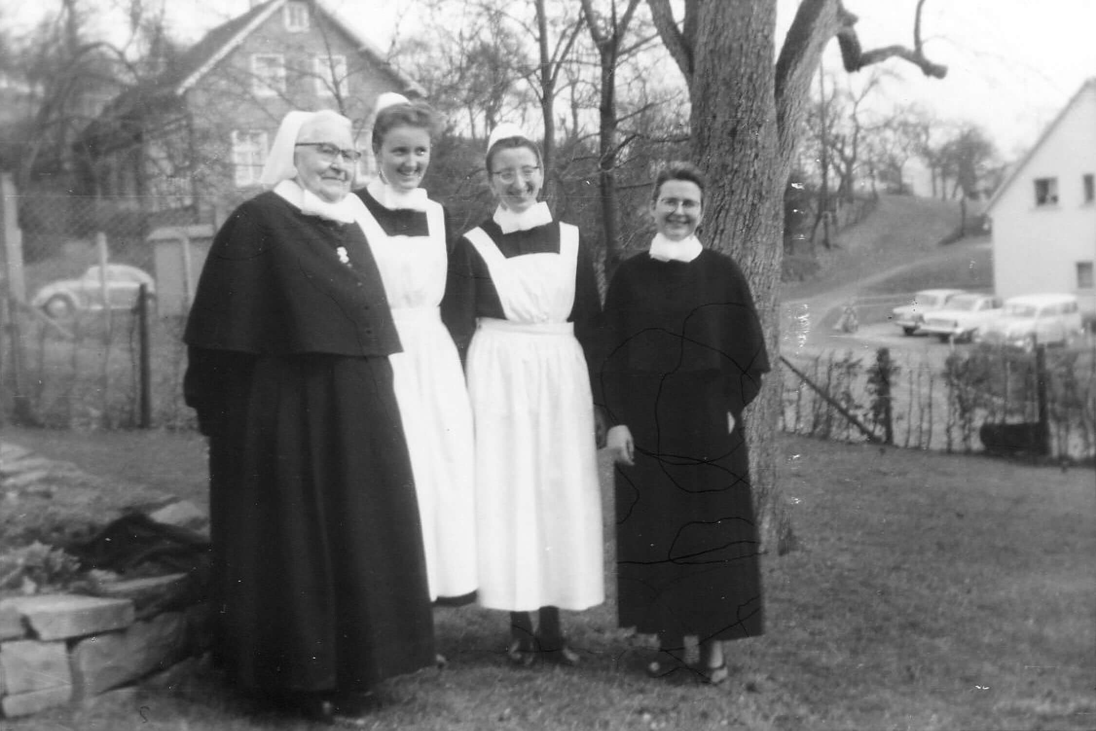 Schwarz-Weiß Foto: Die junge Erika Lüllau lächelt in ihrer Tracht mit drei weiteren Diakonissen. An diesem Tag beginnt für sie ein neues Leben in der Diakonie.