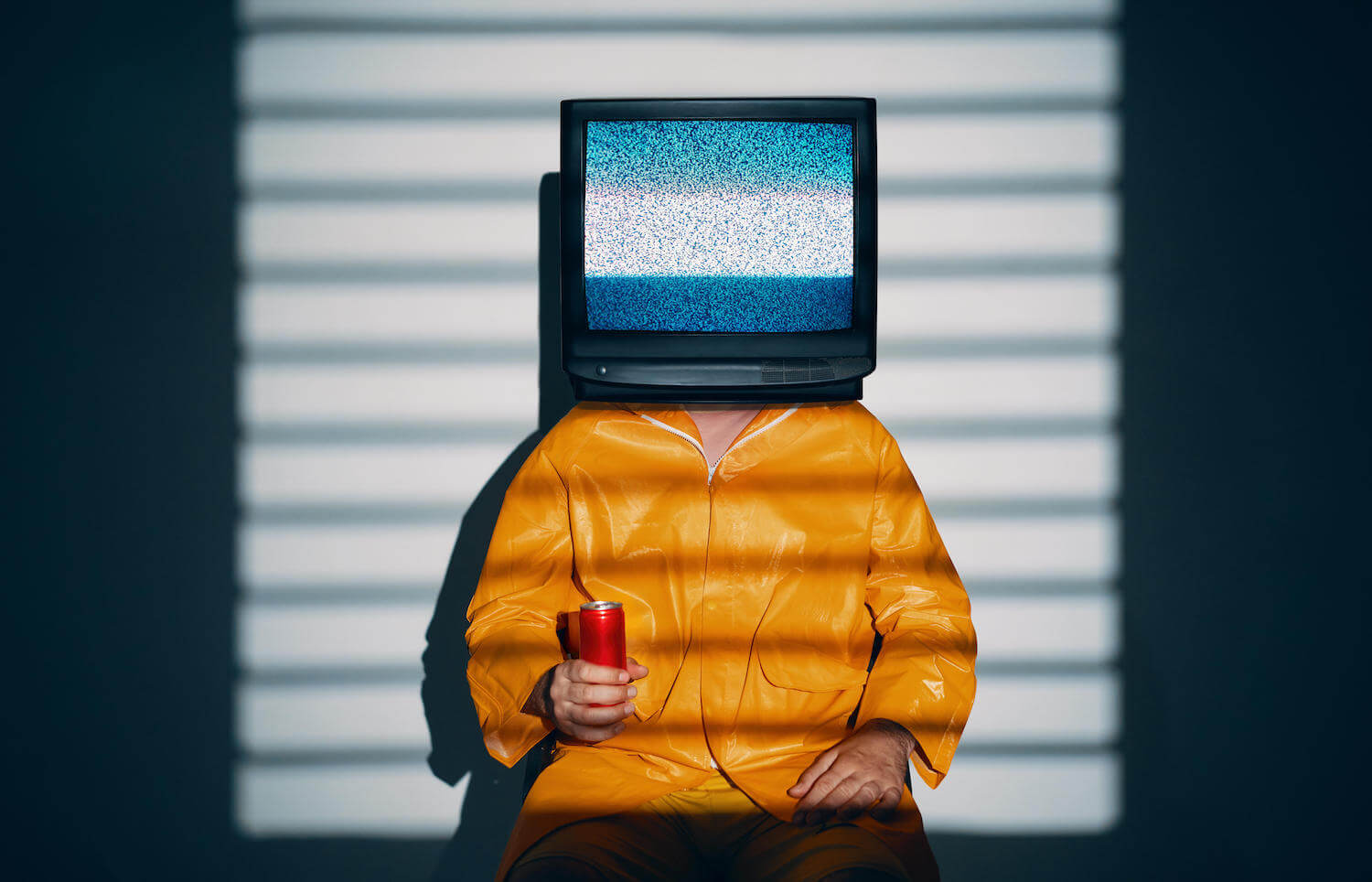 Ein Mann in einem gelben Overal mit einem Fernsehen auf dem Kopf.