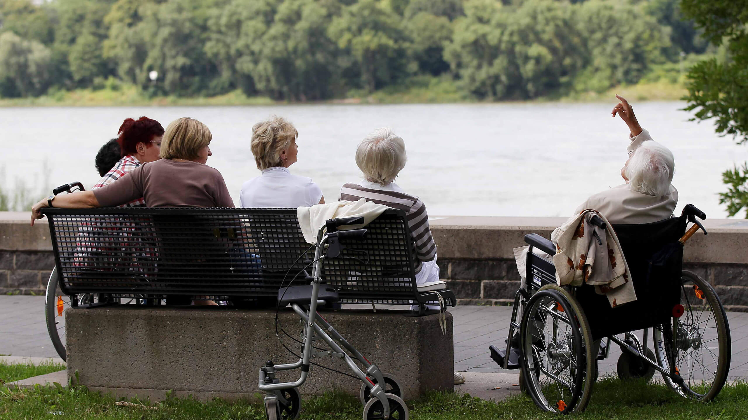 Ältere Menschen auf einer Bank und im Rollstuhl am Kölner Rheinufer