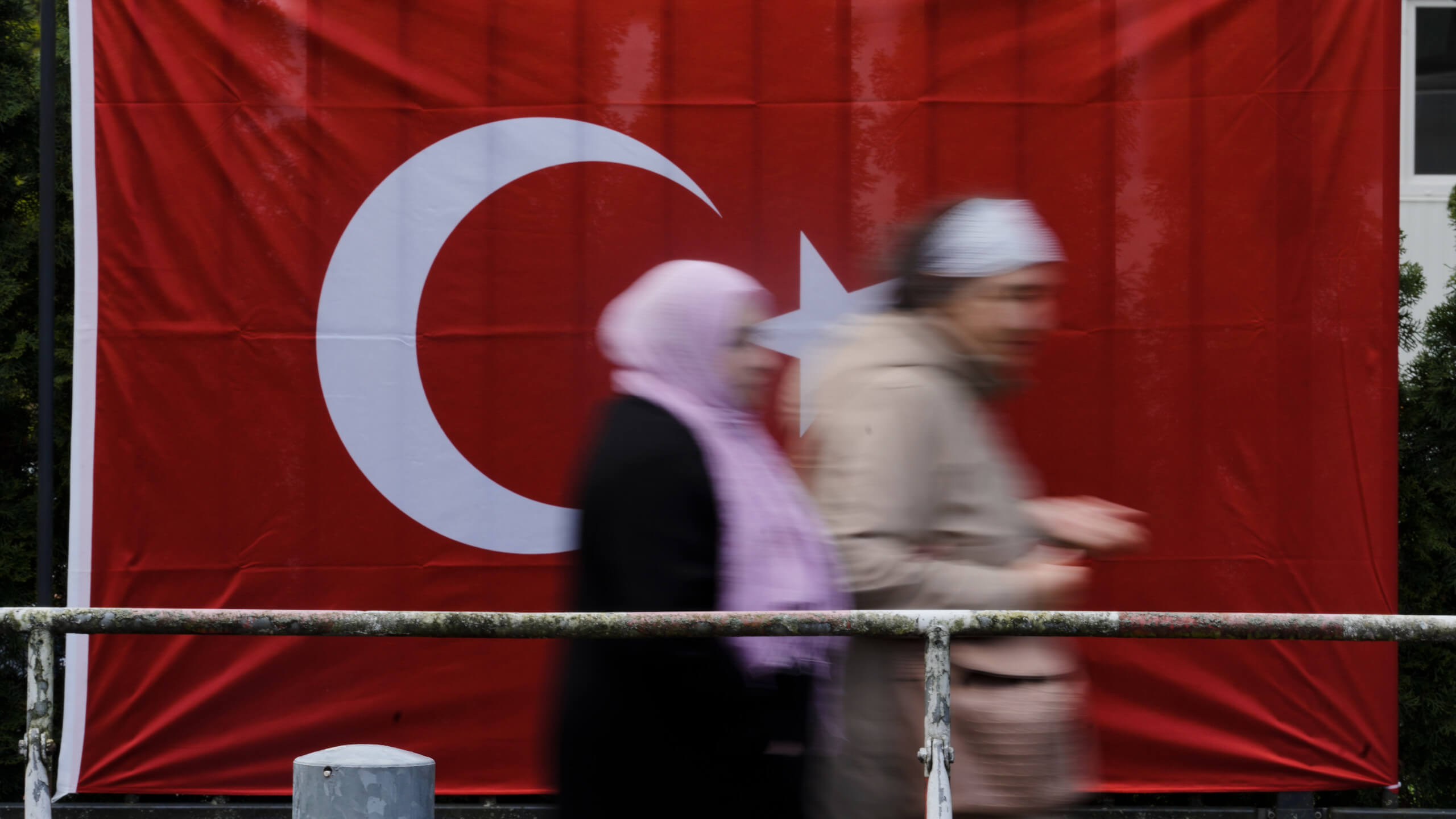 Wählerinnen und Wähler laufen in der Türkei an der türkischen Flagge vorbei
