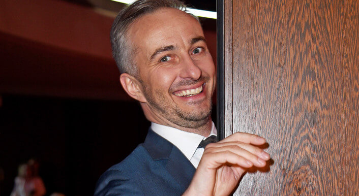 Jan Böhmermann schaut lächelnd hinter einer Tür hervor