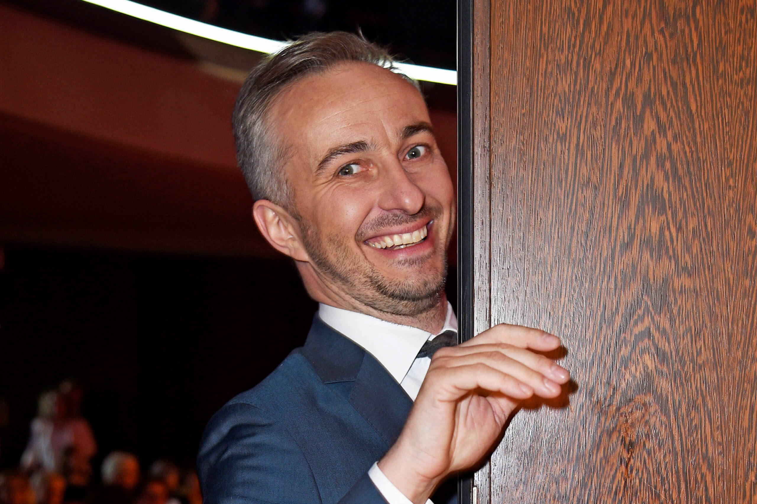 Jan Böhmermann schaut lächelnd hinter einer Tür hervor