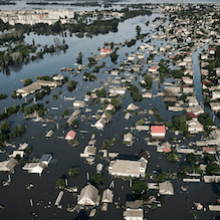 Eine Luftaufnahme zeigt eine ganze Stadt, die unter Wasser steht, nur die Dächer der Häuser ragen hervor.