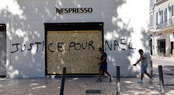 Menschen in Frankreich laufen an einer Wand vorbei mit dem Graffiti „Justice pour Nael“