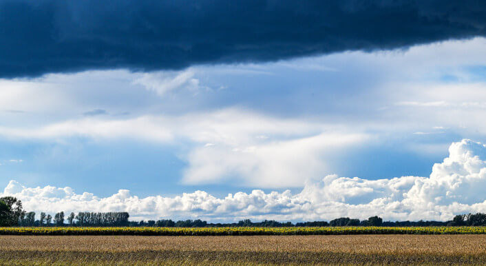 Dunkle Wolken und Abschnitte mit blauem Himmel über einem Feld