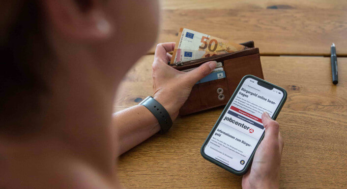 Person hält ein Smartphone, das ein Webseite der Bundesagentur für Arbeit zeigt.