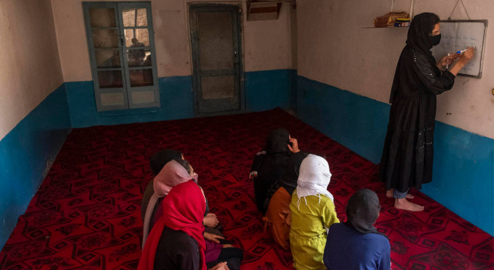 Mehrere Mädchen sitzen auf dem Boden einer geheimen Schule, eine Lehrerin steht an einer Tafel
