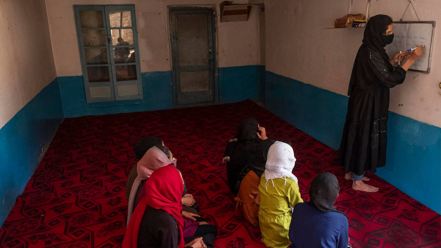 Mehrere Mädchen sitzen auf dem Boden einer geheimen Schule, eine Lehrerin steht an einer Tafel