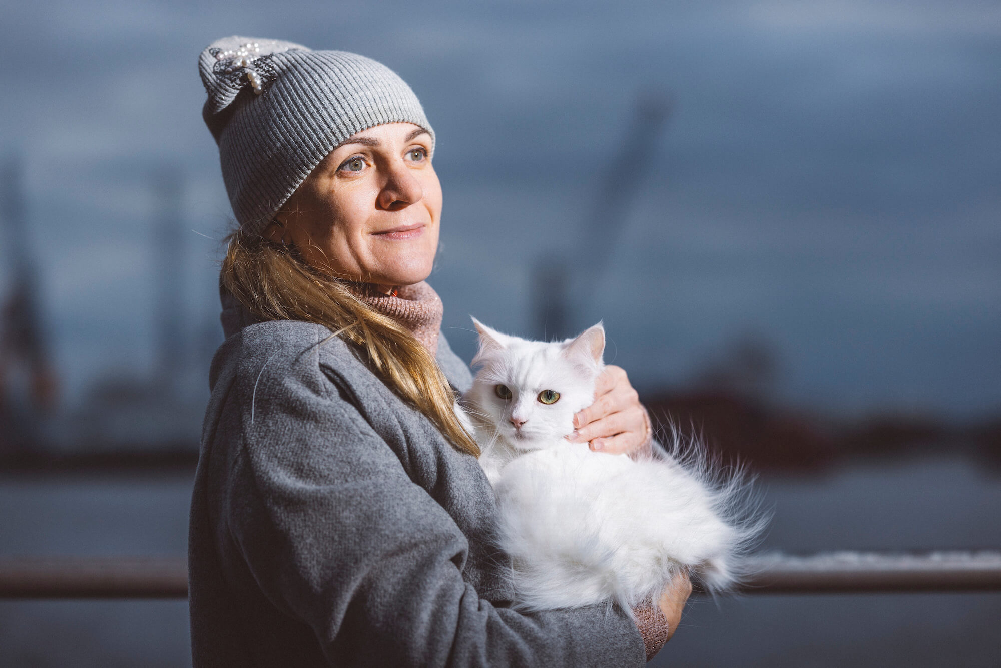 Yuliia Hubina steht mit ihrer Katze auf dem Arm vor der Kulisse des Hamburger Hafens.