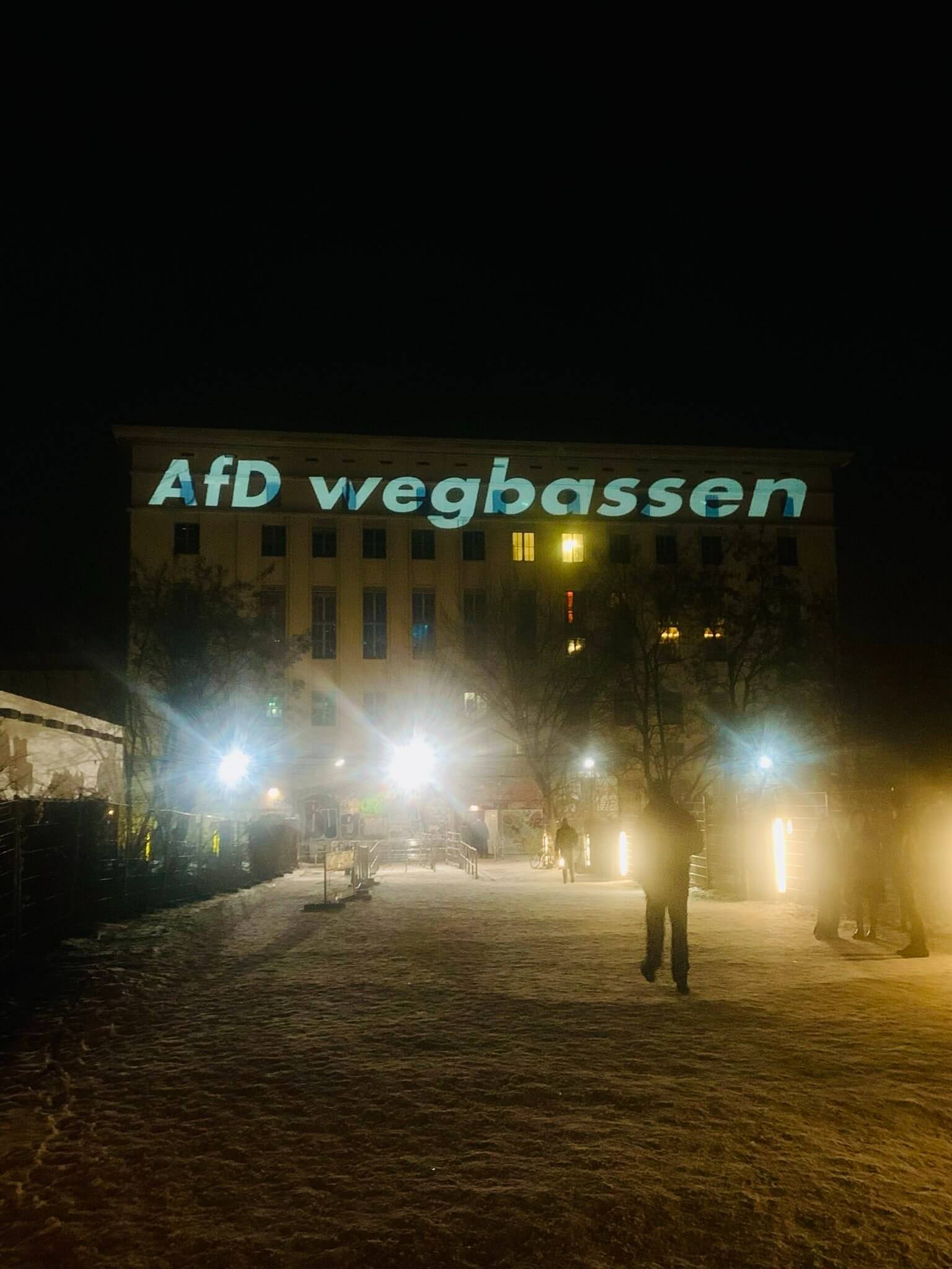 Auf einem verschneiten Weg ist in der Entfernung das Bunker-Gebäudes des Berghain-Clubs zu sehen mit einer großen Projekten mit dem Titel: „AfD wegbassen"