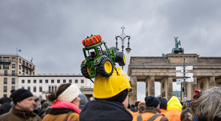 Vor dem Brandenburger Tor wird protestiert, ein Mann trägt einen kleinen Traktor auf dem Kopf.