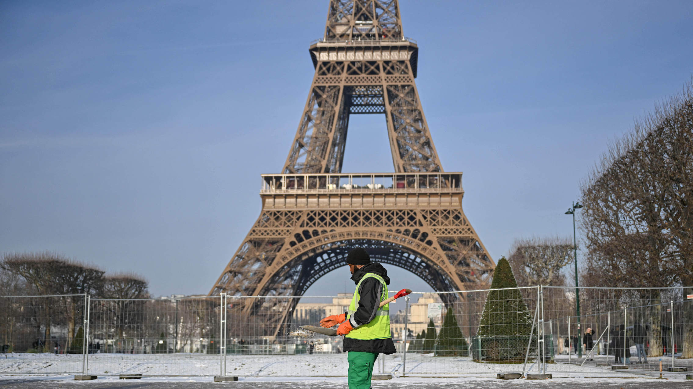 Eiffelturm bei Schnee und ein Arbeiter in Paris, der die Bürgersteige gegen den Frost streut, am 18. Januar 2024