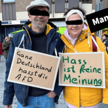 Ein Foto zeigt zwei Demonstrierende nebeneinander. Eine Person trage ein Schild, auf dem steht: „Ganz Deutschland hasst die AfD“, die andere eines mit: „Hass ist keine Meinung“.
