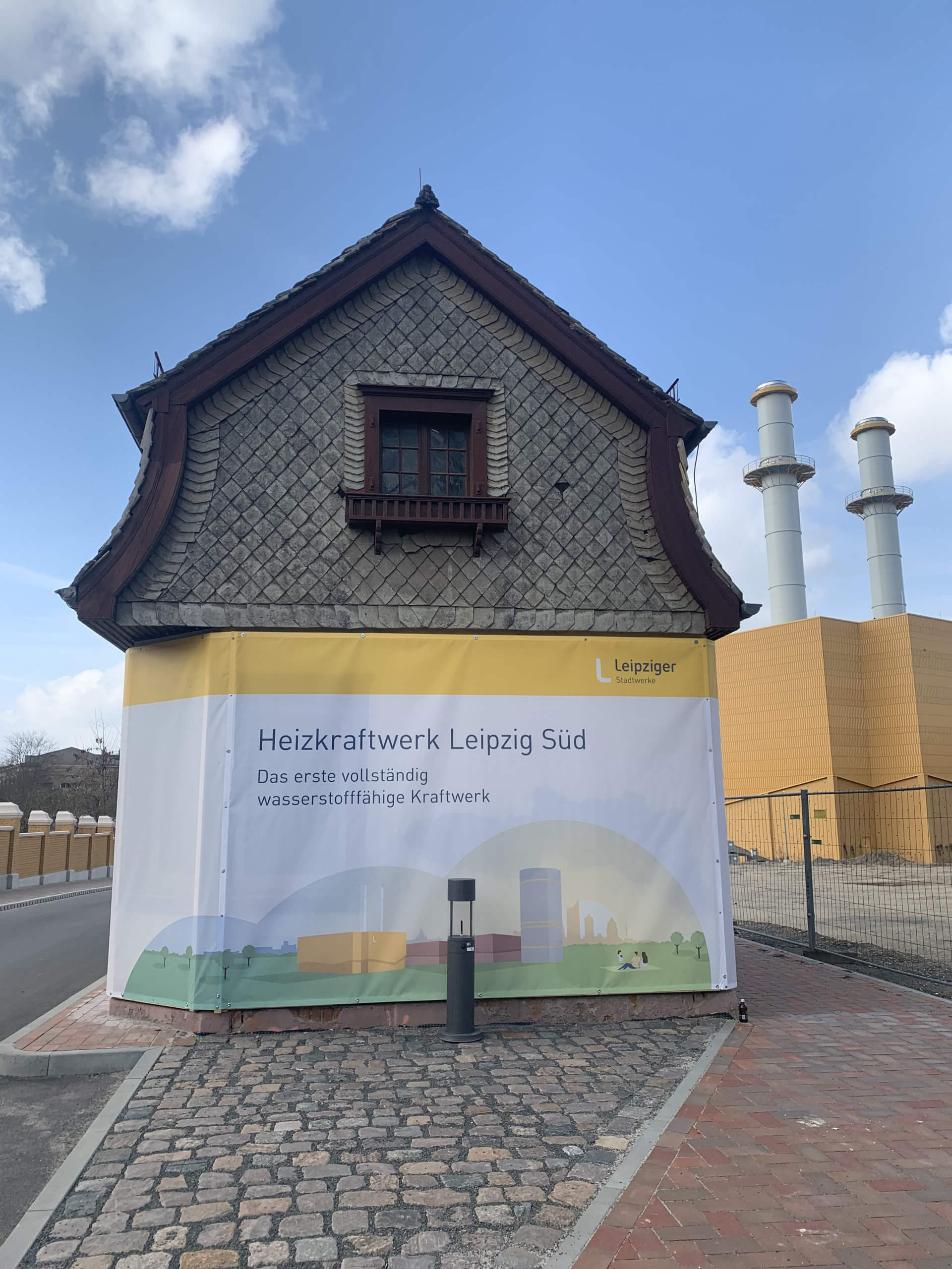 Das Foto zeigt ein Plakat, was am Eingang des Heizkraftwerk Leipzig Süd hängt. Es bewirbt die Anlage als „erstes vollständig wasserstofffähiges Kraftwerk“. 