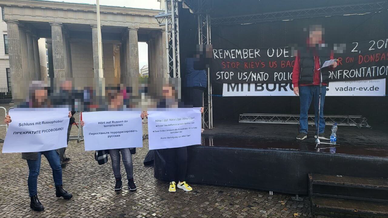 Drei Frauen stehen mit Plakaten in der Hand vor einer Bühne vor dem Brandenburger Tor – im Hintergrund das Logo der Organisation Vadar