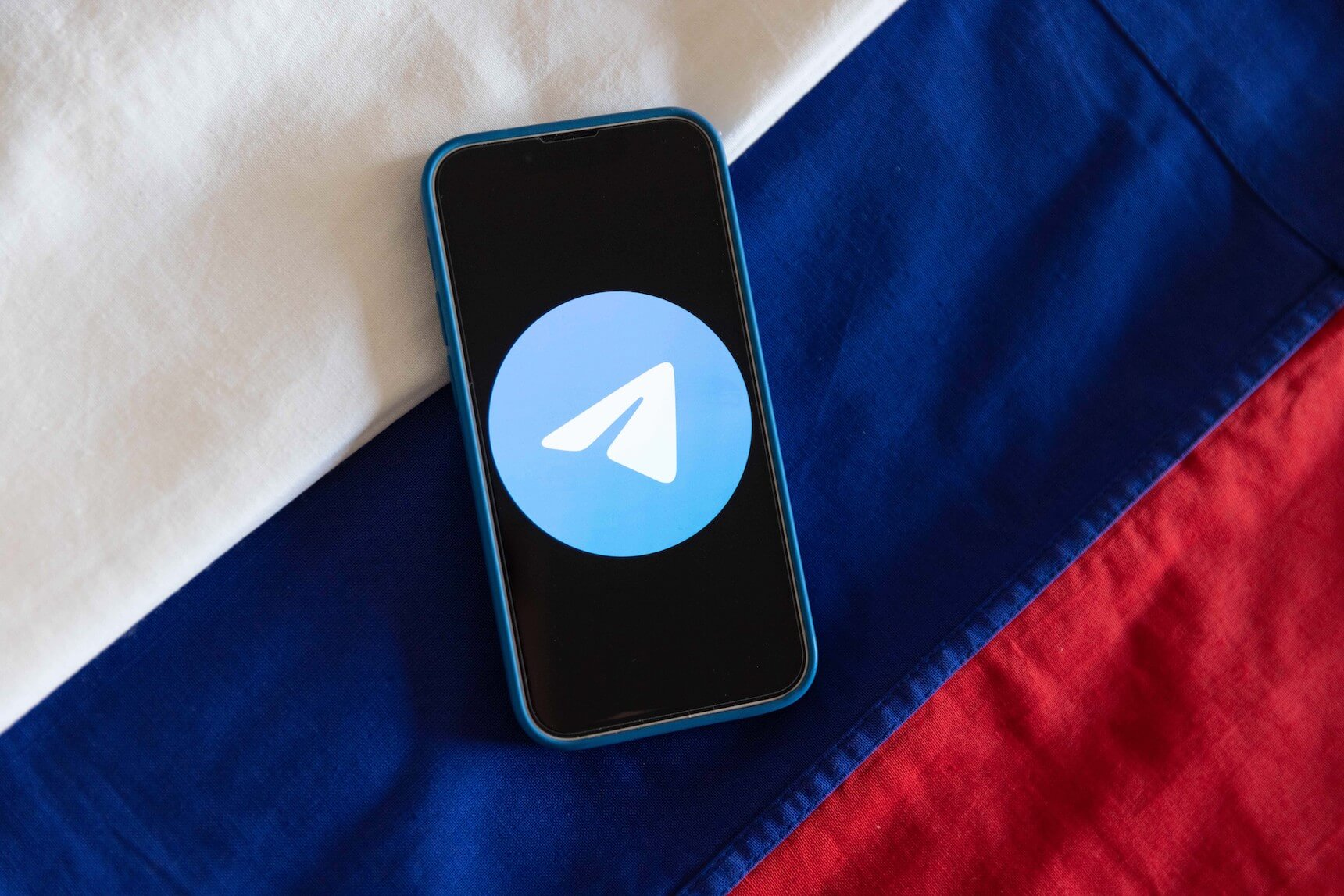 Smartphone mit Telegram-Logo auf dem Bilschirm, im Hintergund eine Russland Flagge
