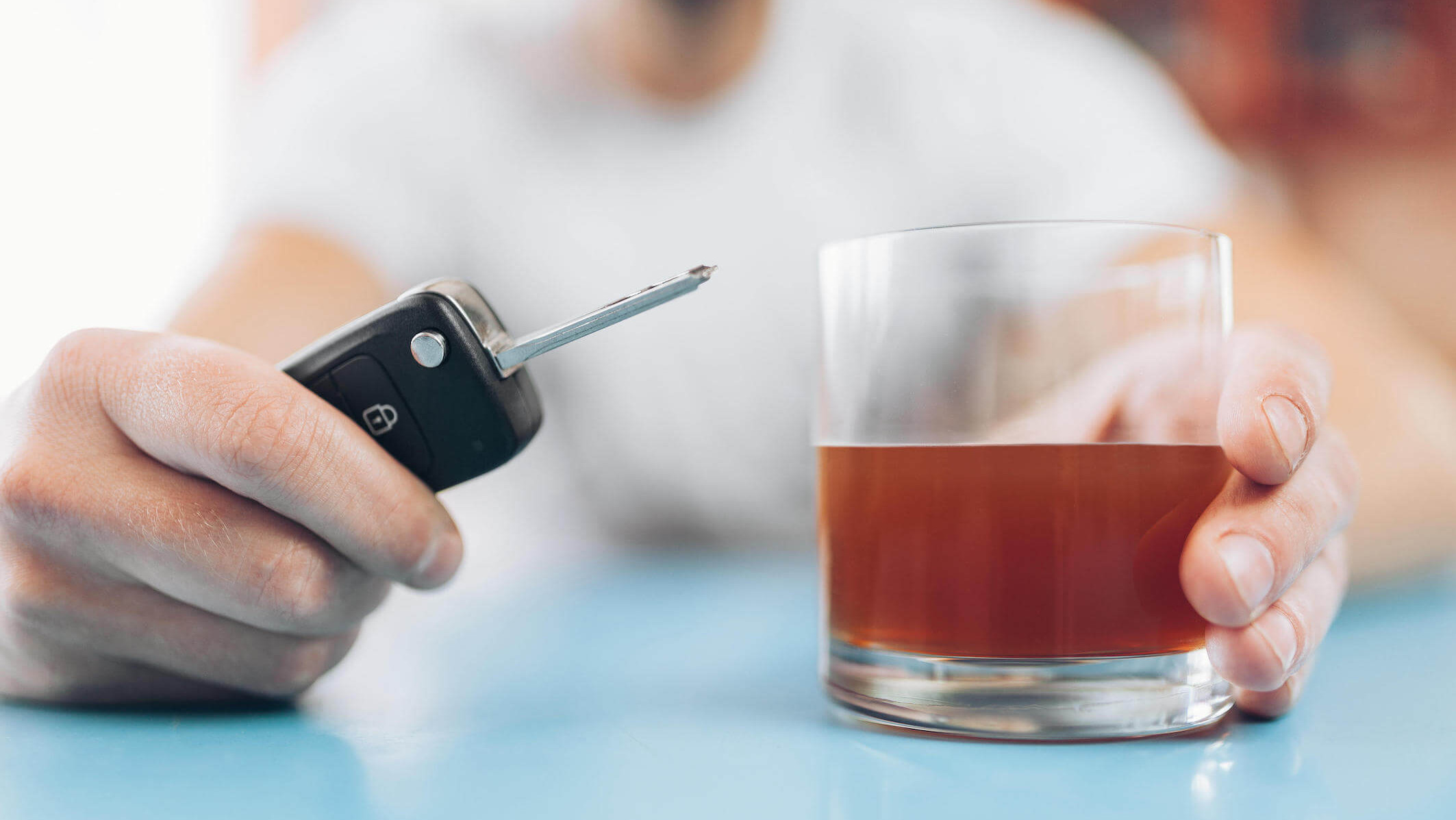 Eine Person an einem Tisch, verschwommen, sie hält einen Autoschlüssel und ein alkoholisches Getränk im Glas in der Hand