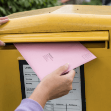 Eine Person wirft einen Briefwahl-Umschlag in einen Briefkasten.