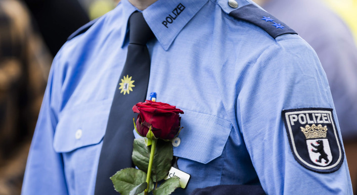 Ein Polizist in Uniform hält eine rote Rose.