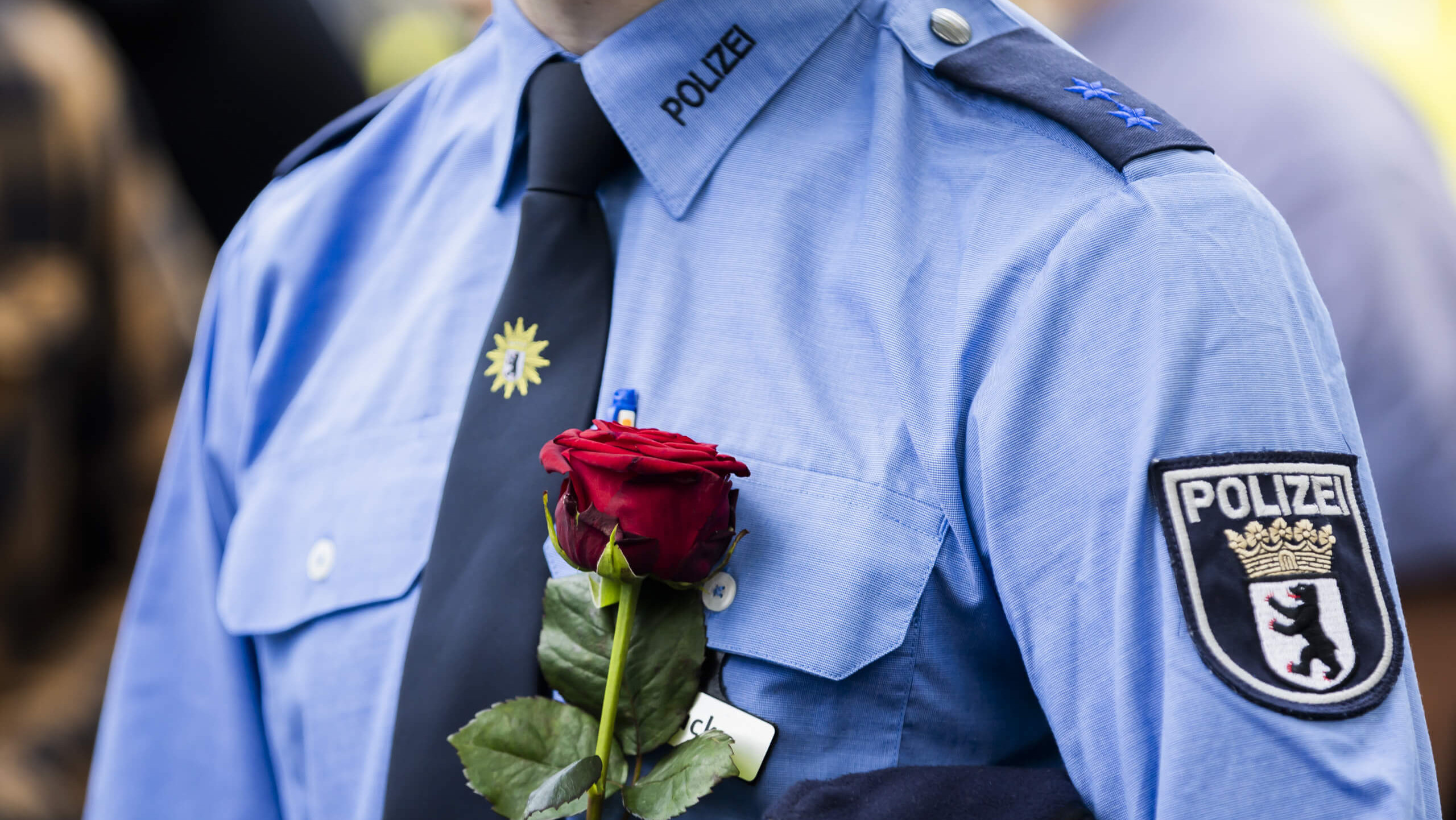 Ein Polizist in Uniform hält eine rote Rose.