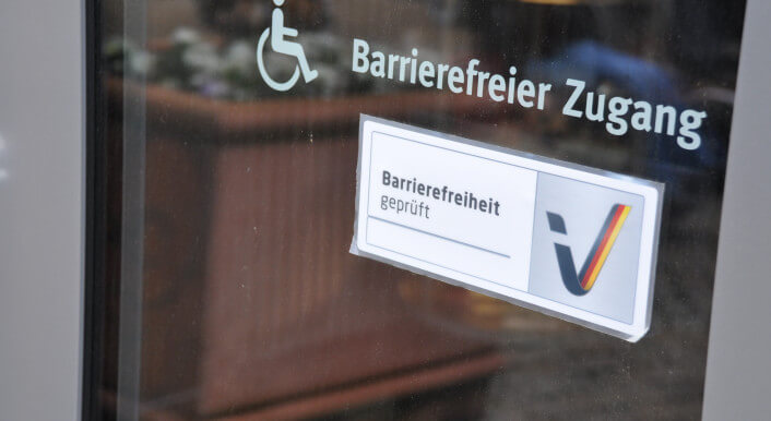 Ein Aufdruck auf einer Glastür zu einem Raum zeigt an: Der Raum hinter der Tür bietet einen barrierefreien Zugang.