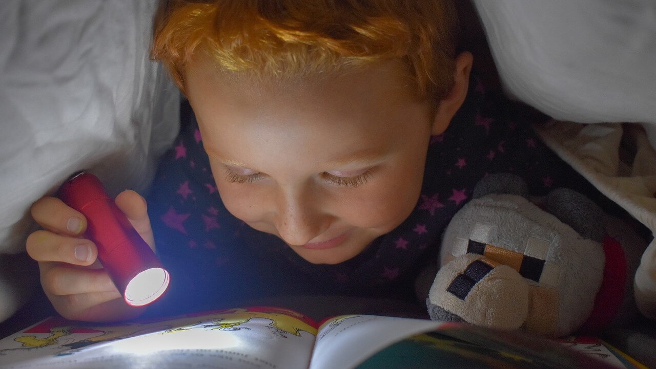Kind liest unter der Bettdecke mit einer Taschenlampe.