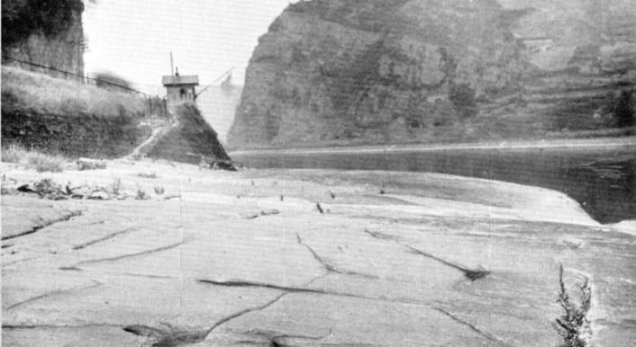 Dünner Wasserstrom schlängelt sich durch ein trockenes Flussbett – im Hintergrund sind ein Berg und ein Turm zu sehen
