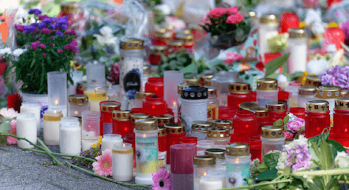 Kerzen und Blumen stehen auf dem Asphalt.