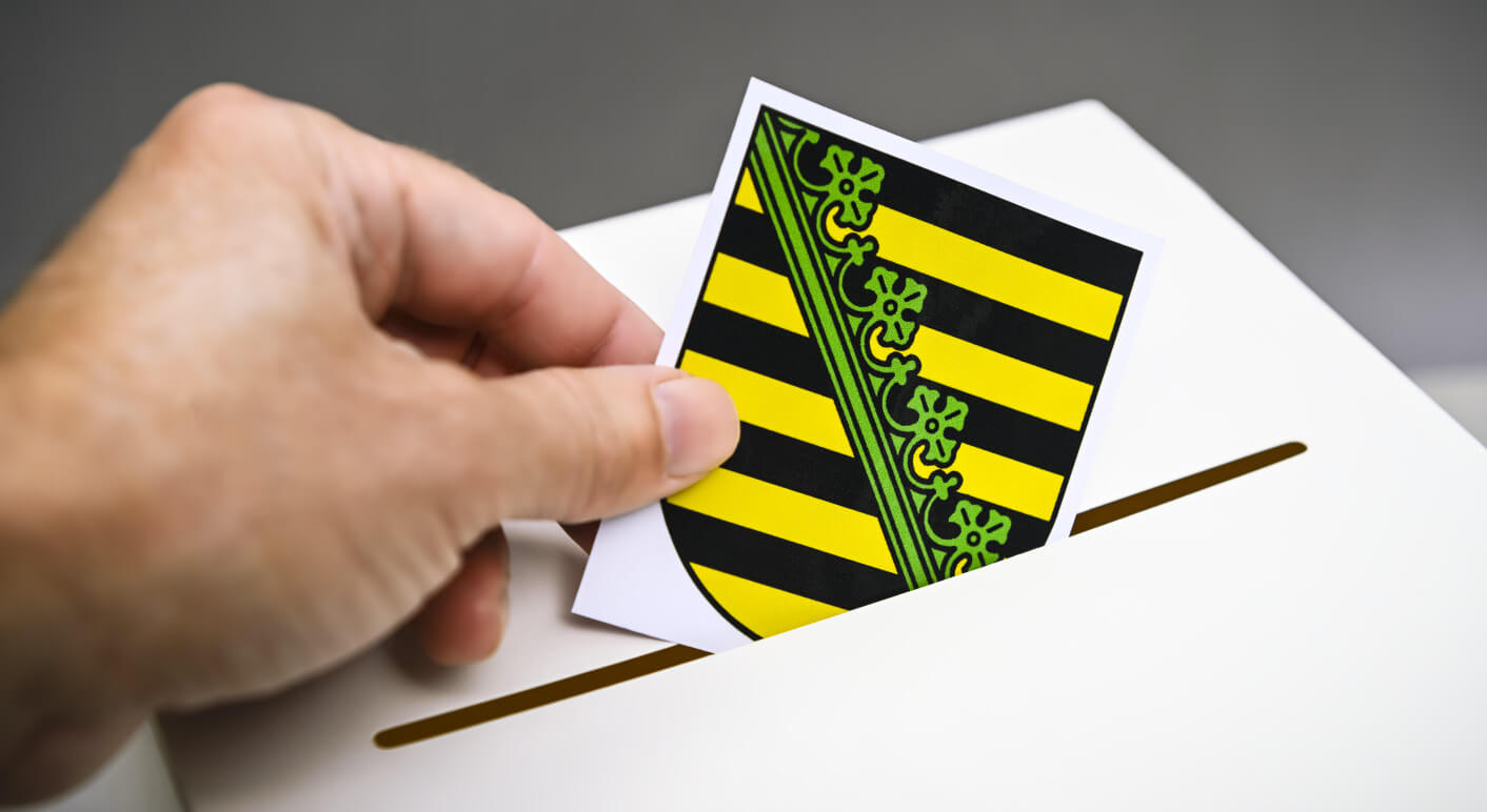 Das Wappen von Sachsen wird in eine Wahlbox geworfen, Symbolfoto Landtagswahl in Sachsen