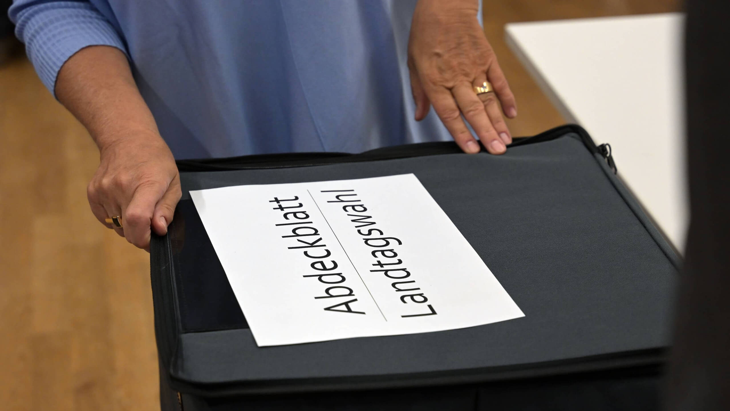 Mann legt ein A4-Blatt mit der Aufschrift Abdeckblatt Landtagswahl auf eine Wahlurne aus Stoff mit Reißverschluss