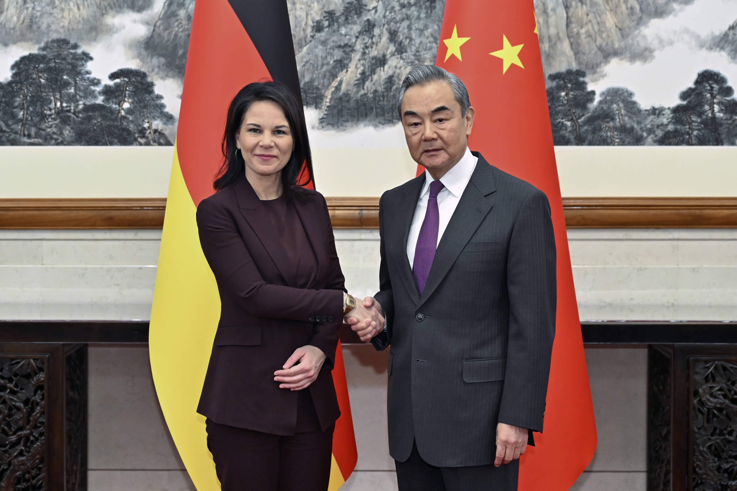 Annalena Baerbock gibt dem chinesischen Außenminister Wang Yi vor Nationalflaggen die Hand