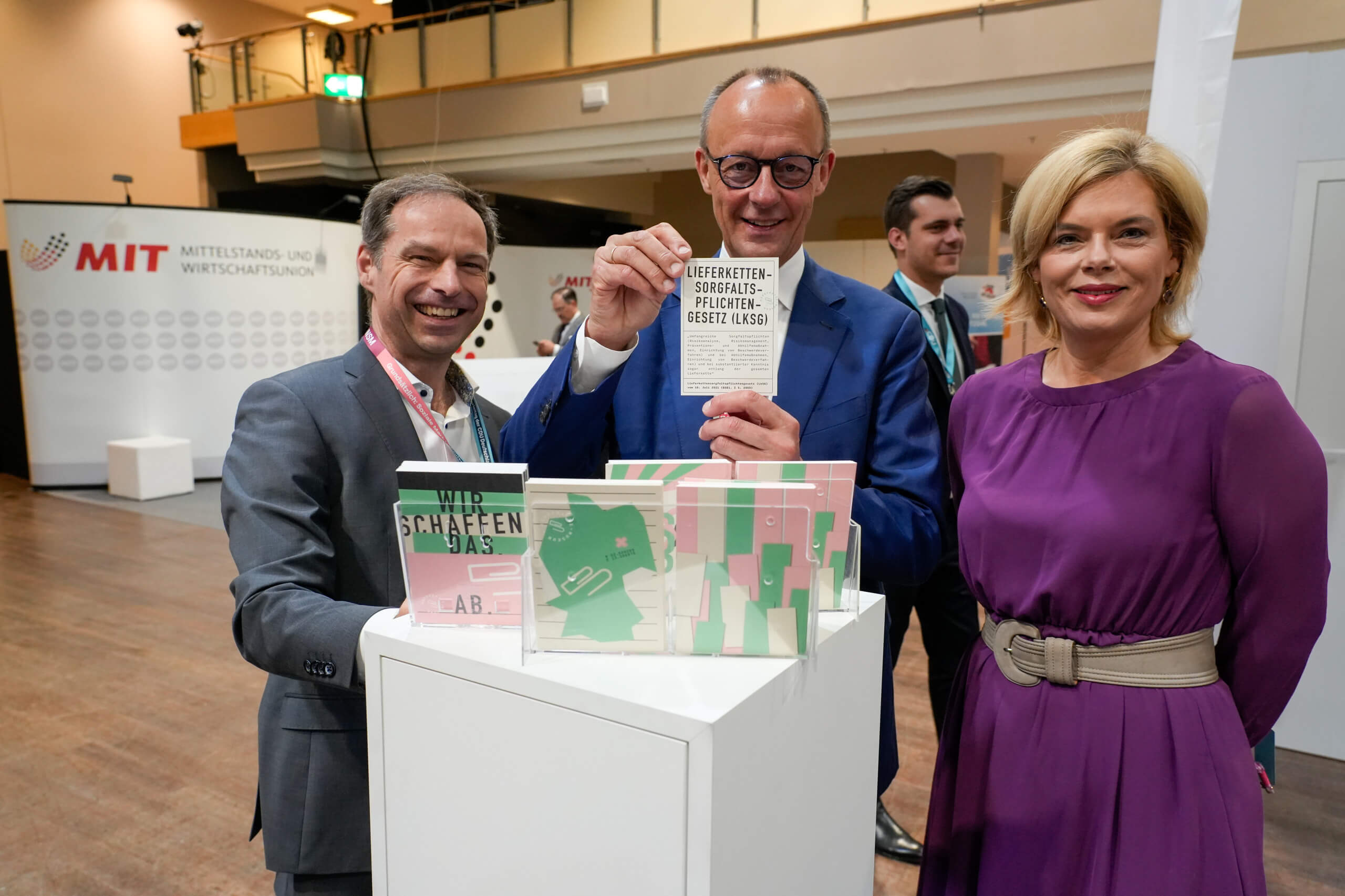 Thorsten Alsleben, Friedrich Merz und Julia Klöckner stehen vor einem Schredder und Merz hält ein Papier mit der Aufschrift "Lieferkettensorgfaltspflichtengesetz" hoch.