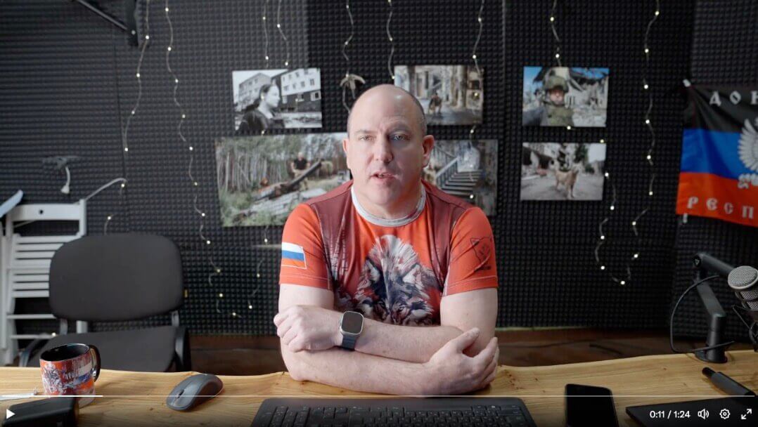 Dougan sitting on a desk - pictures hanging on the wall behind him 