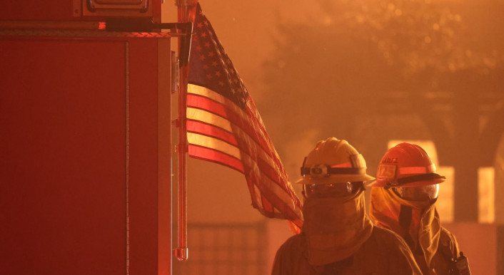 Zwei Feuerwehrkräfte neben einem Wagen und US-Flagge umgeben von gelbem Rauch