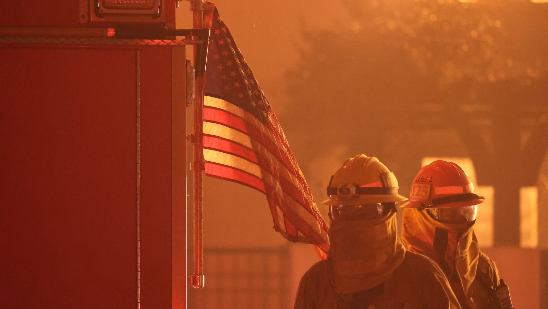 Zwei Feuerwehrkräfte neben einem Wagen und US-Flagge umgeben von gelbem Rauch