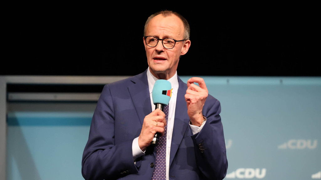 Friedrich Merz im Anzug vor einer blauen Wand mit dem CDU-Logo – mit Mikrofon in der Hand